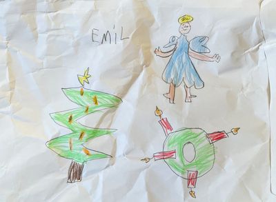 A crumpled envelop with drawings of a christmas tree, a christmas wreath with four candles, an angel, and the lettering of Emil.